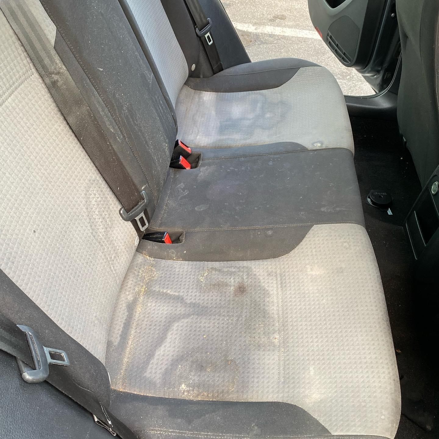 Dirty gray car back seat with visible stains and red seatbelt buckles