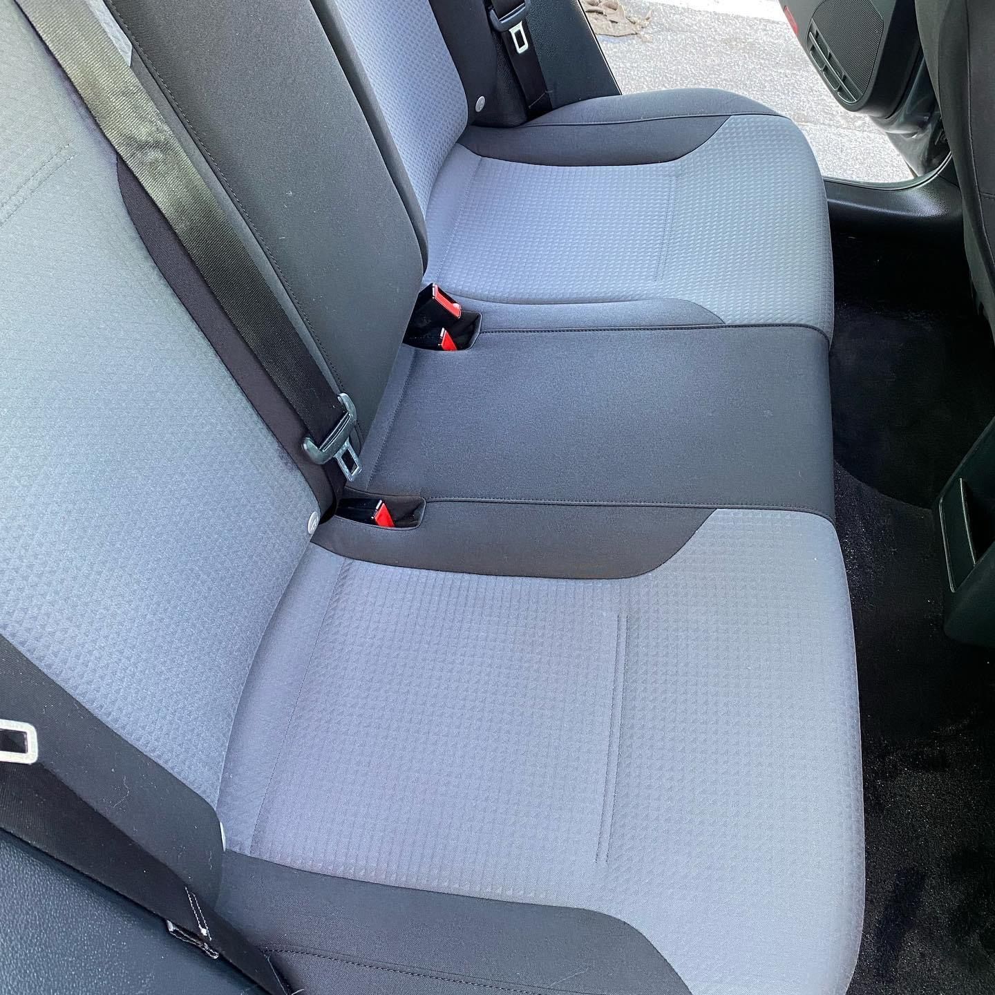 Gray car back seat with two fabric bench cushions and red seat belt buckles