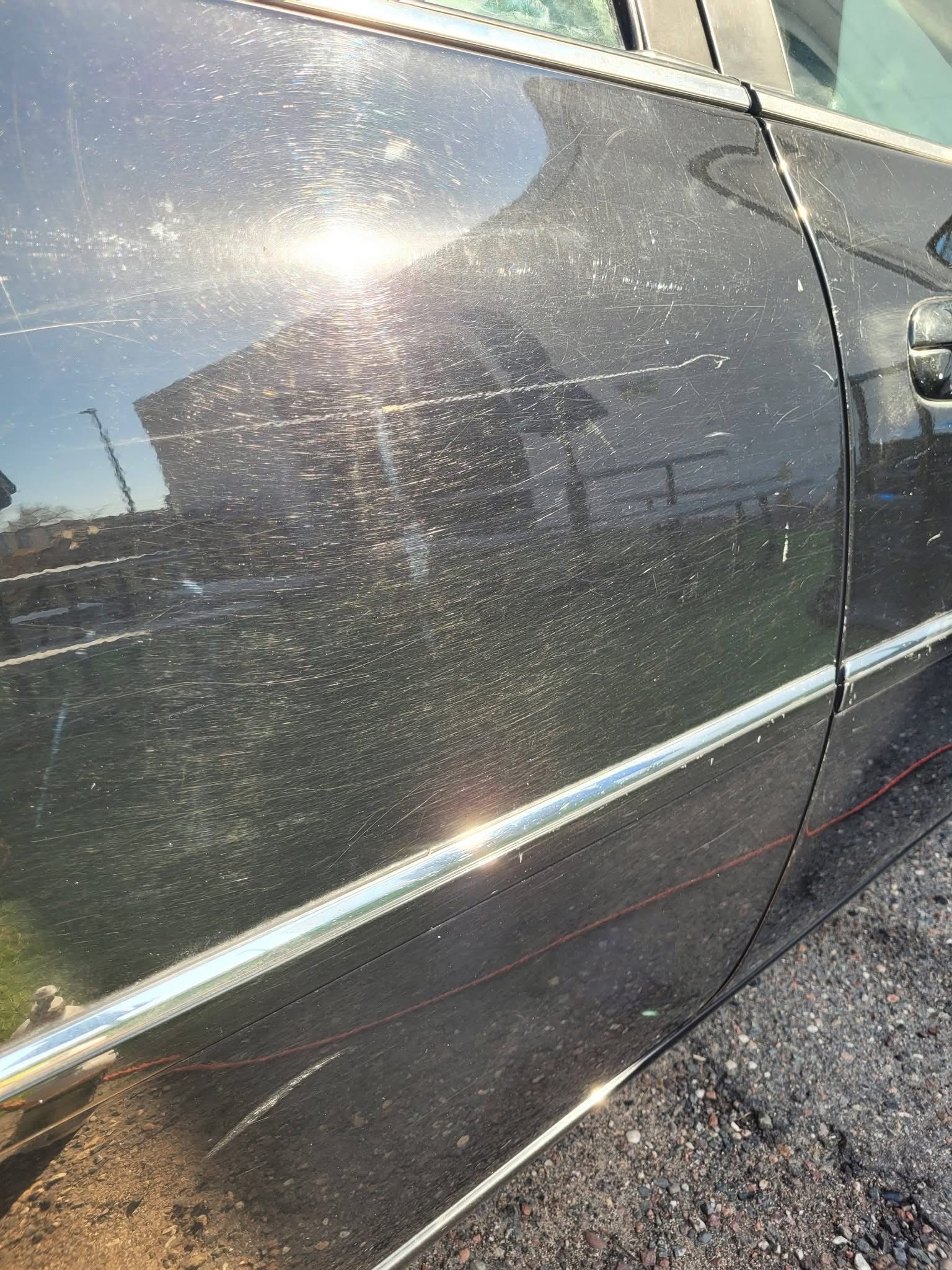 Sun glare reflecting on a black car door with dust and chrome trim outdoors