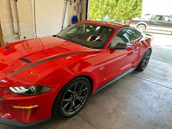 Red Ford Mustang in a garage with a black hood and wheels