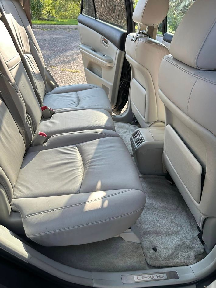 Gray car back seat with folded seat cushion, beige leather front seat, and open door view