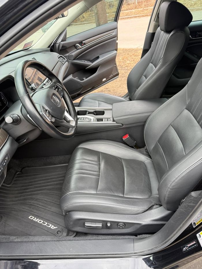 Black leather car interior with open driver’s door and steering wheel visible