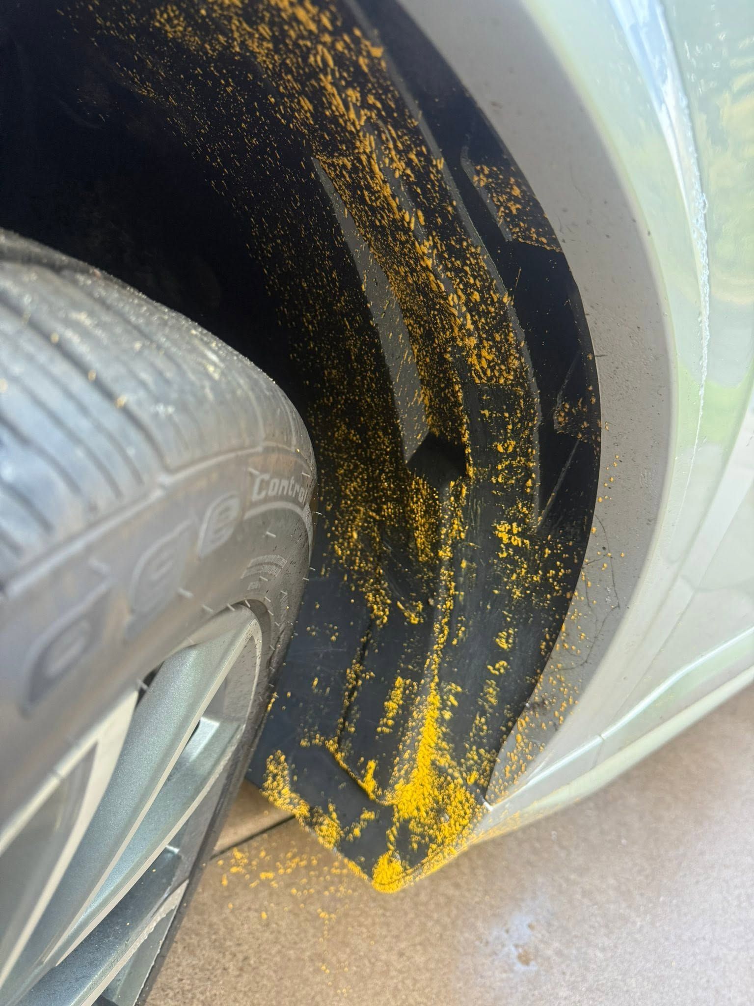 Car tire beside a black mud flap with yellow paint splatter near a curb