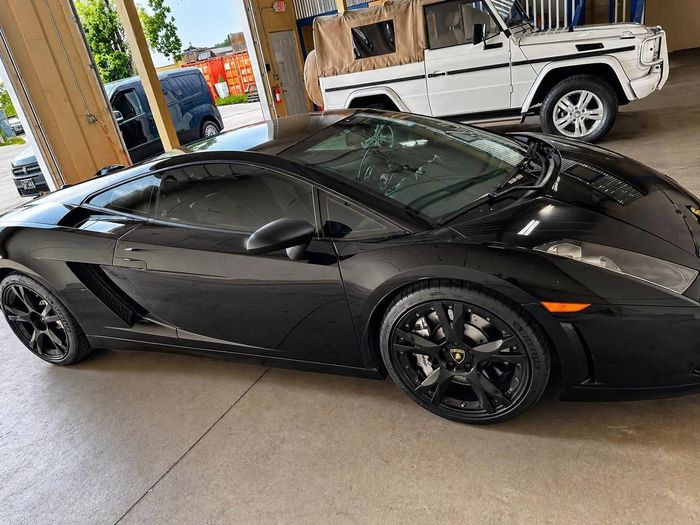 Black sports car parked indoors beside a damaged white SUV.