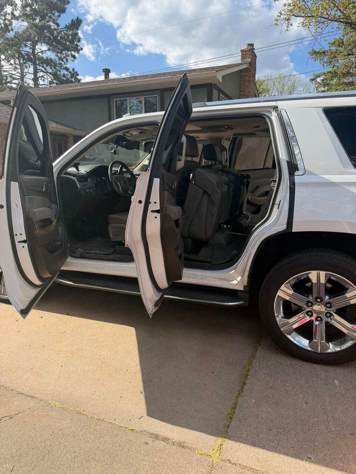 White SUV with both passenger-side doors open in a driveway, showing the interior and front wheel.