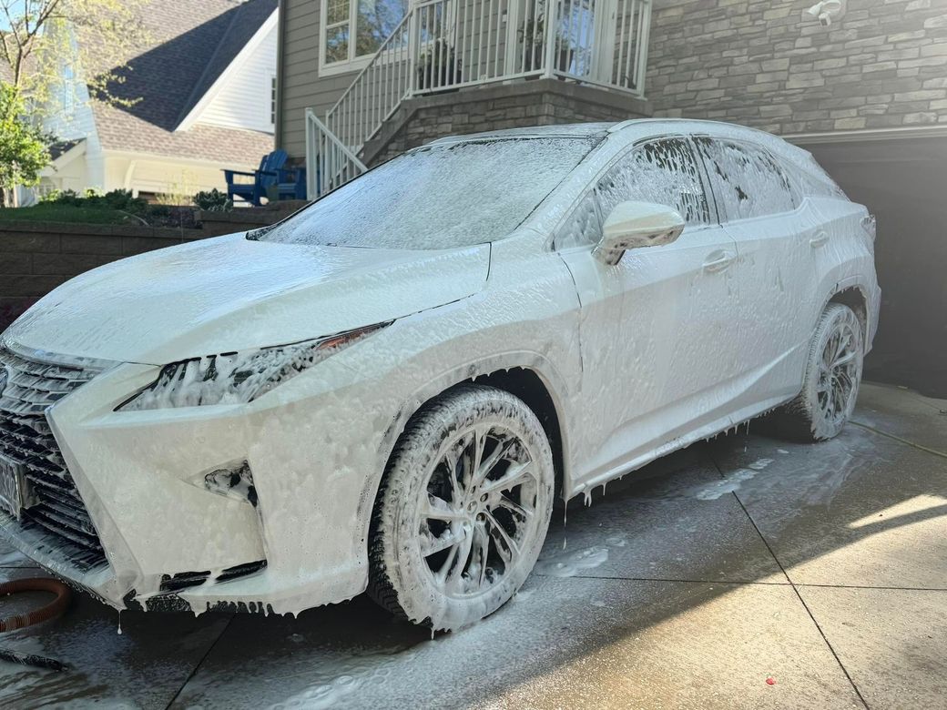 White SUV covered in foam during a car wash in a driveway