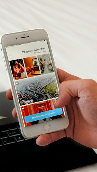 Person's hand holding a smartphone displaying a social media interface with photos and a button.