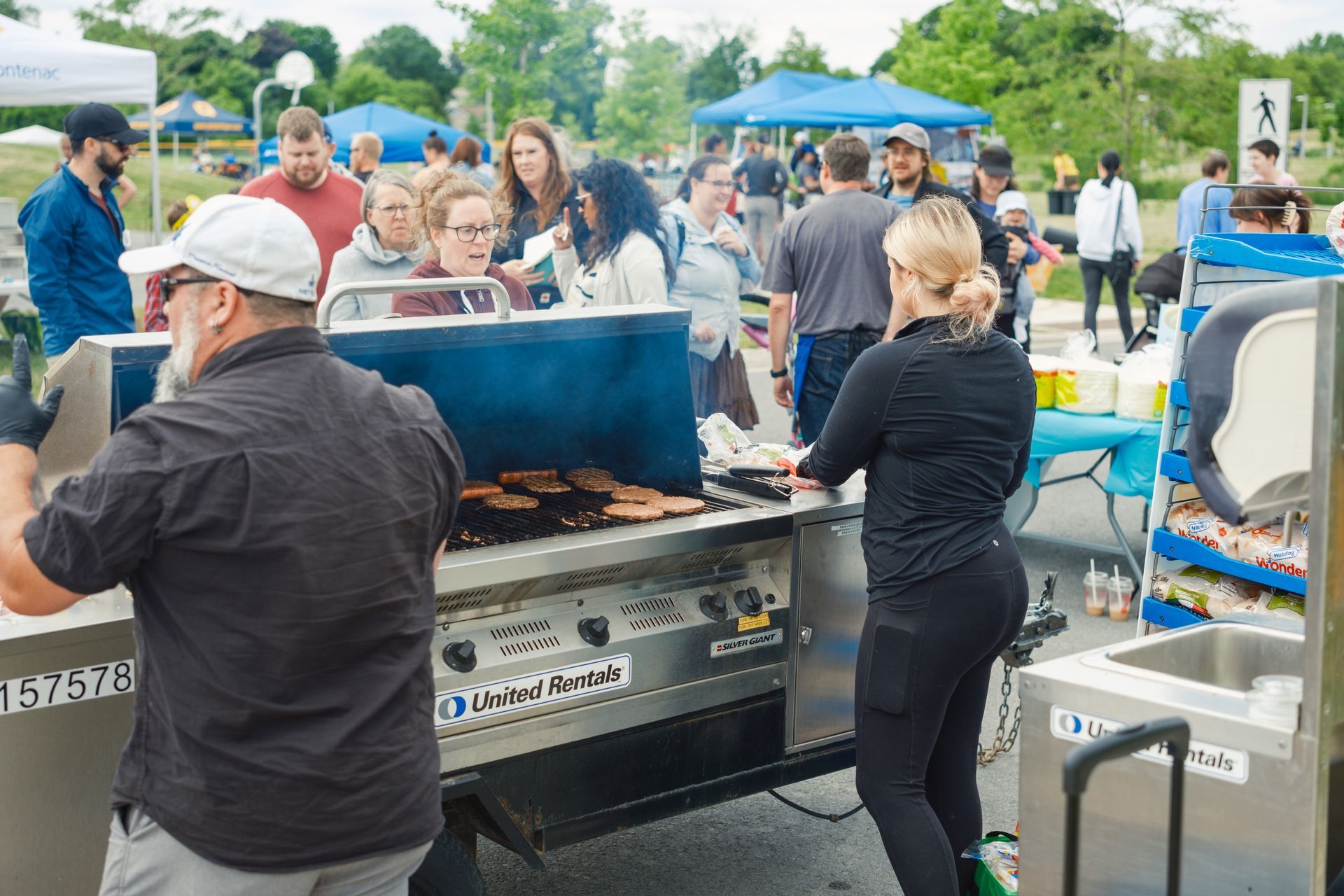 A man and a woman are cooking food on a grill in front of a crowd of people.