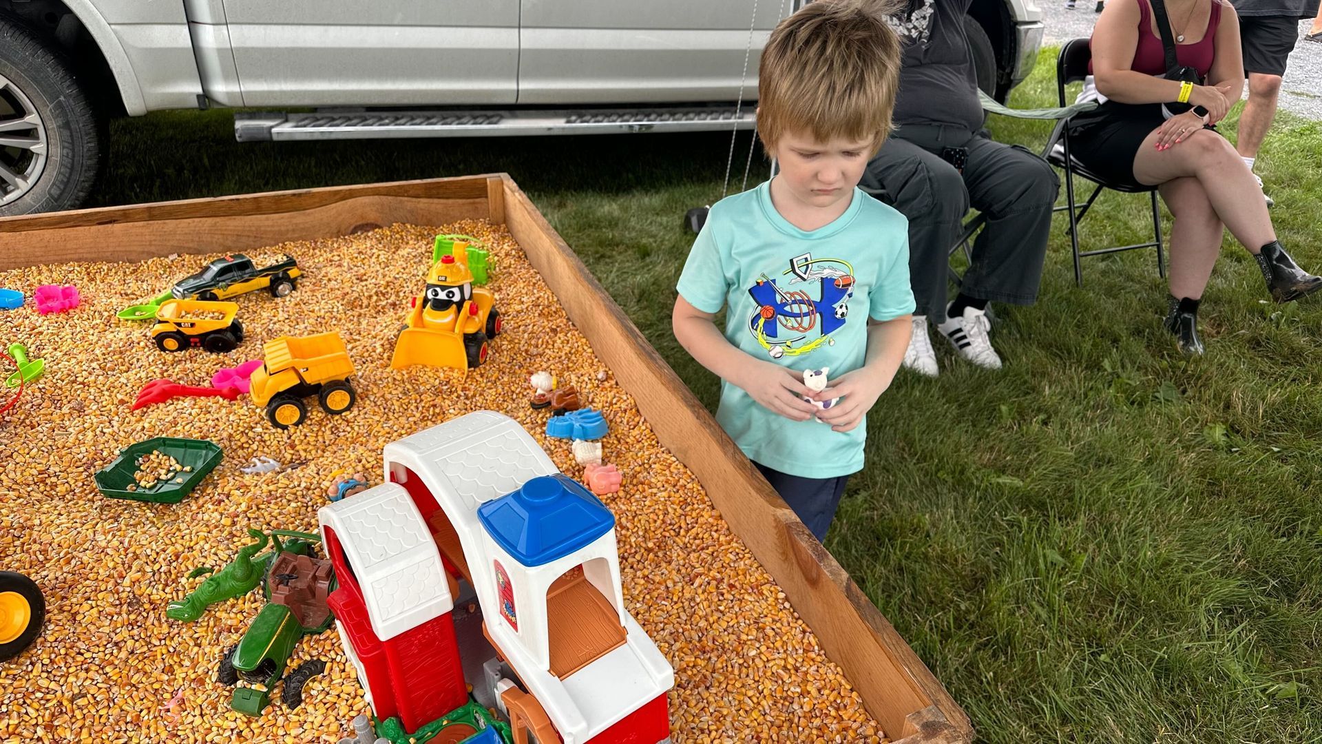 A young boy is standing next to a sandbox filled with toys.