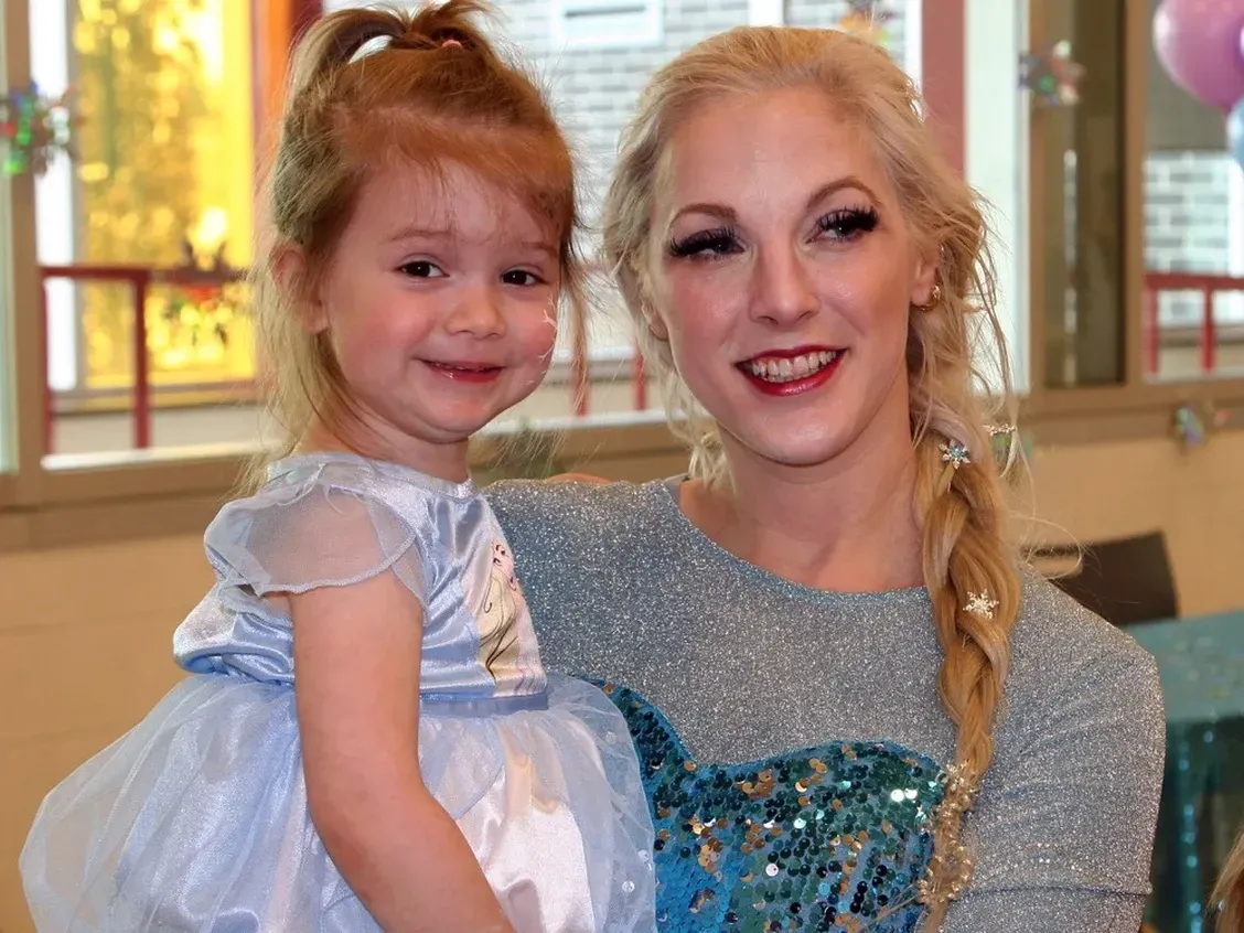 A woman in a frozen costume is holding a little girl in her arms.