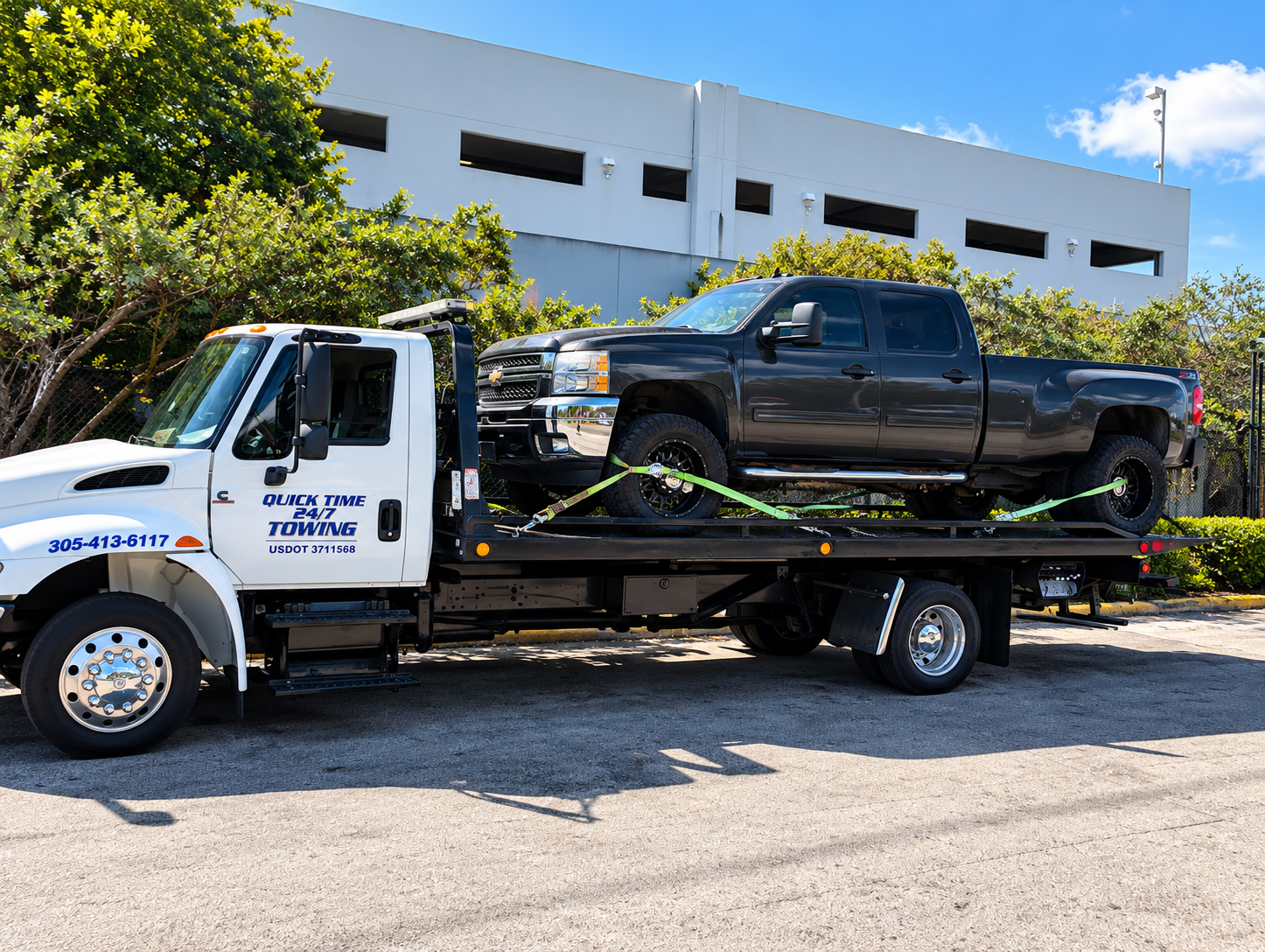 Tow truck carrying a black pickup parked on a flatbed outside a building
