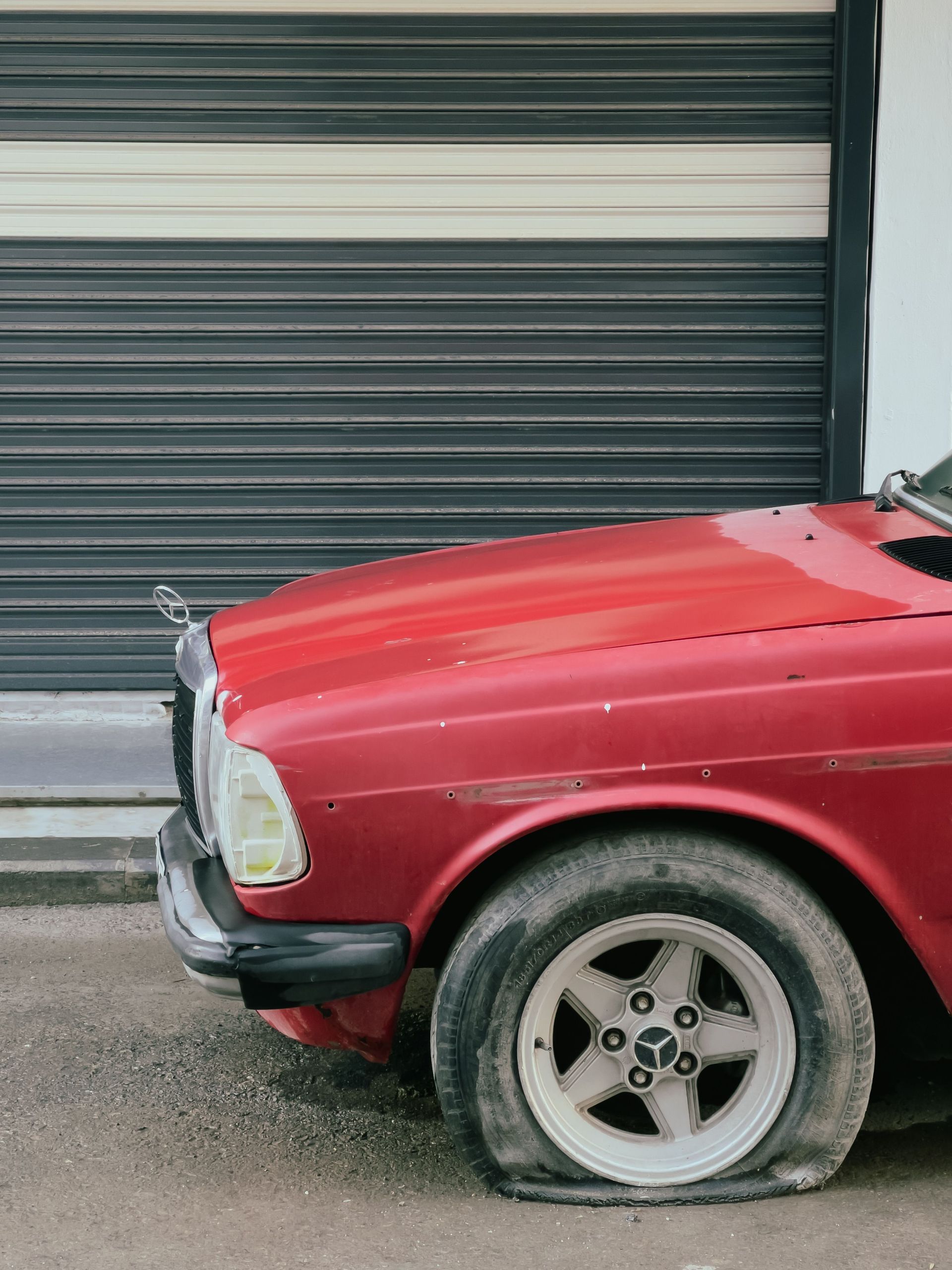 Red car with a damaged front end parked beside a gray garage door.