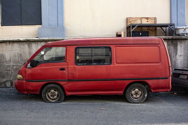 Red cargo van parked beside a wall with blue-trimmed windows.