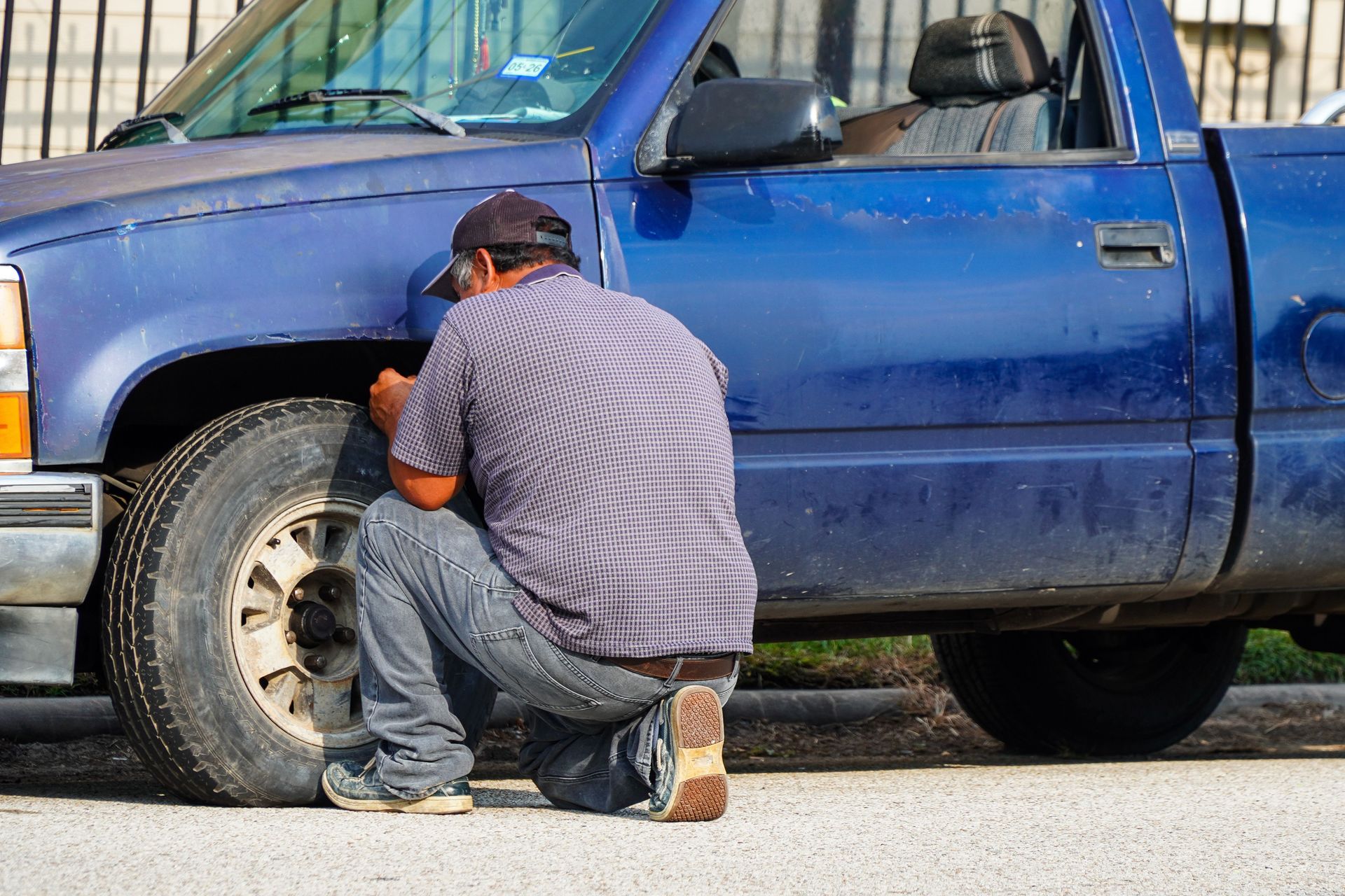 Man kneeling by blue truck, changing a tire on the roadside