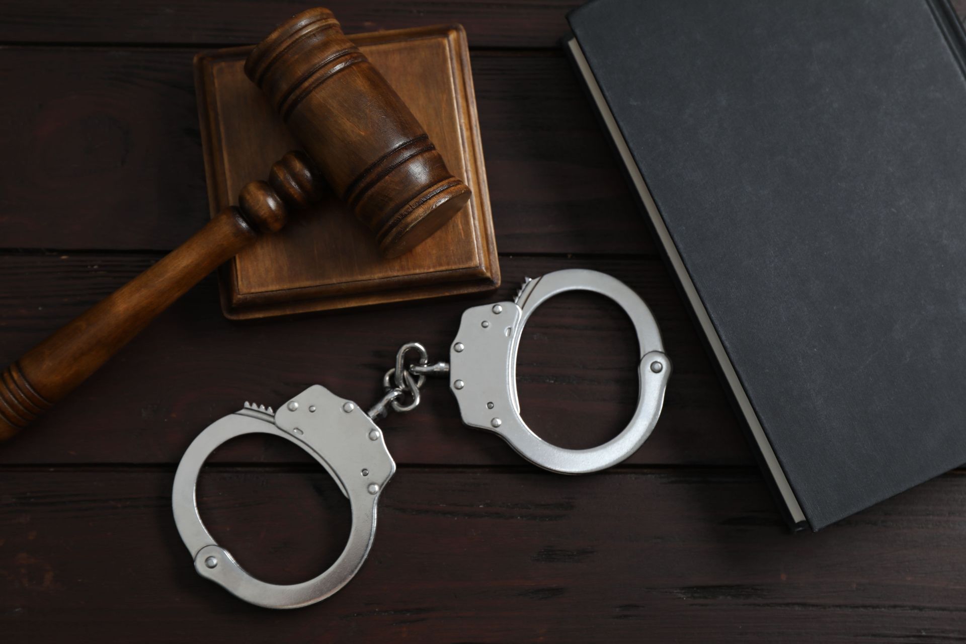 Handcuffs beside a judge’s gavel on a dark desk with a closed black folder