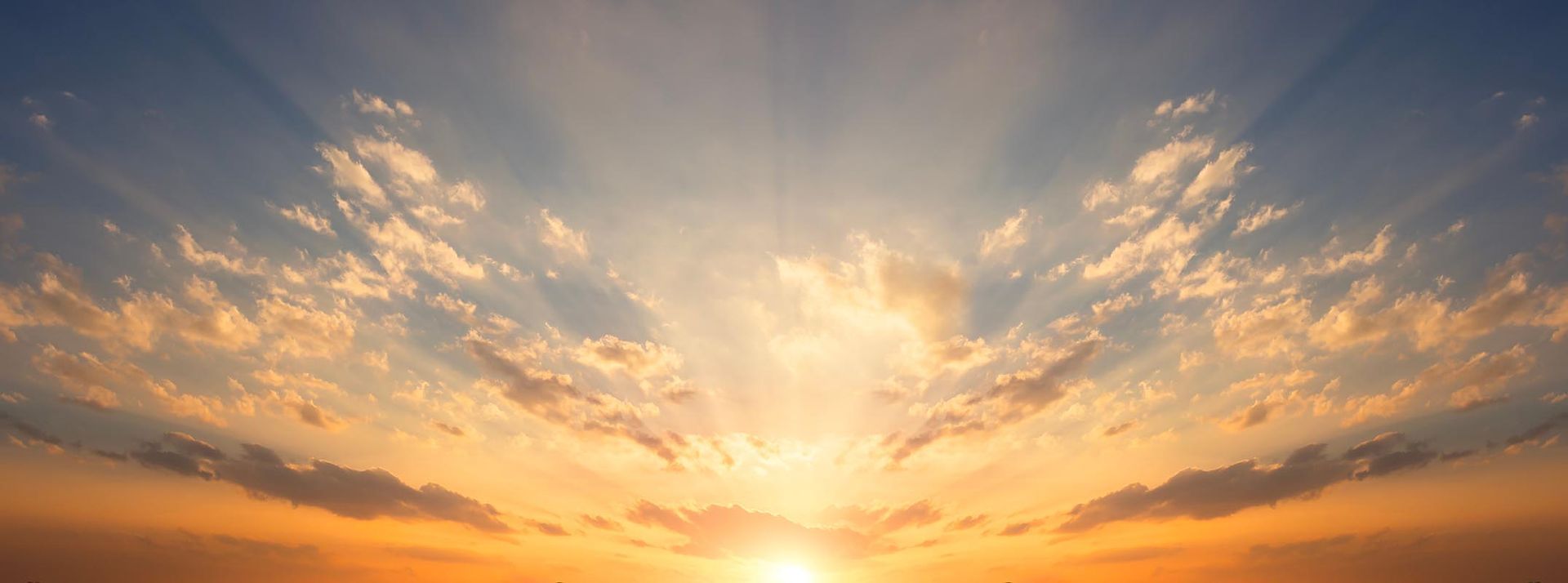 A vibrant sunrise with golden light radiating through scattered clouds in a blue and orange sky.