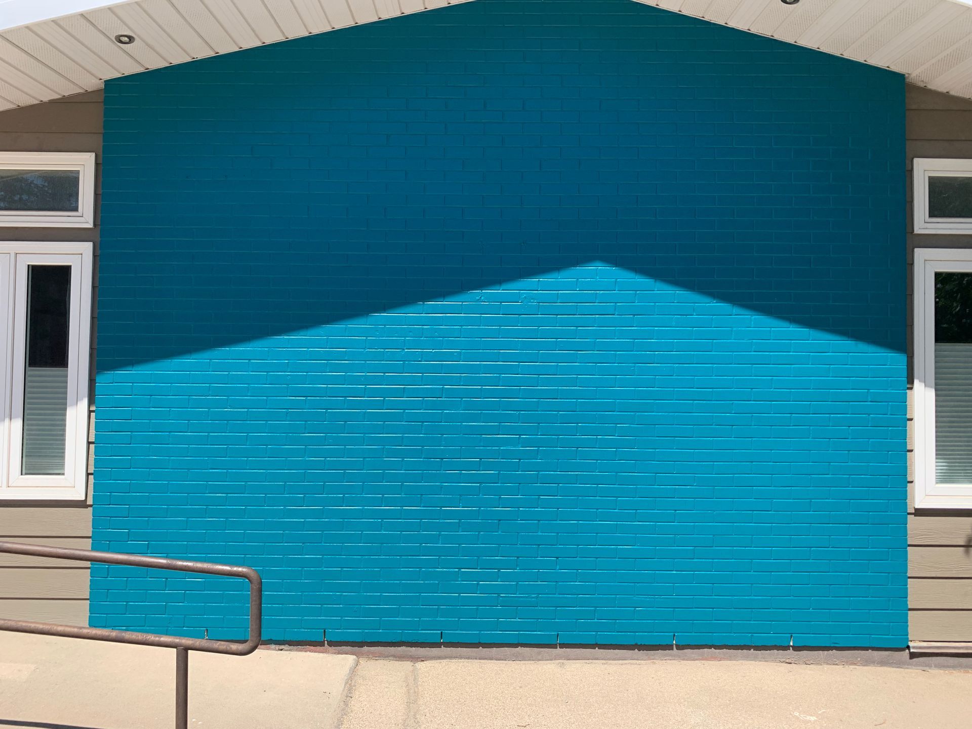 Bright blue building wall with a lighter blue triangular reflection, flanked by white-framed windows.