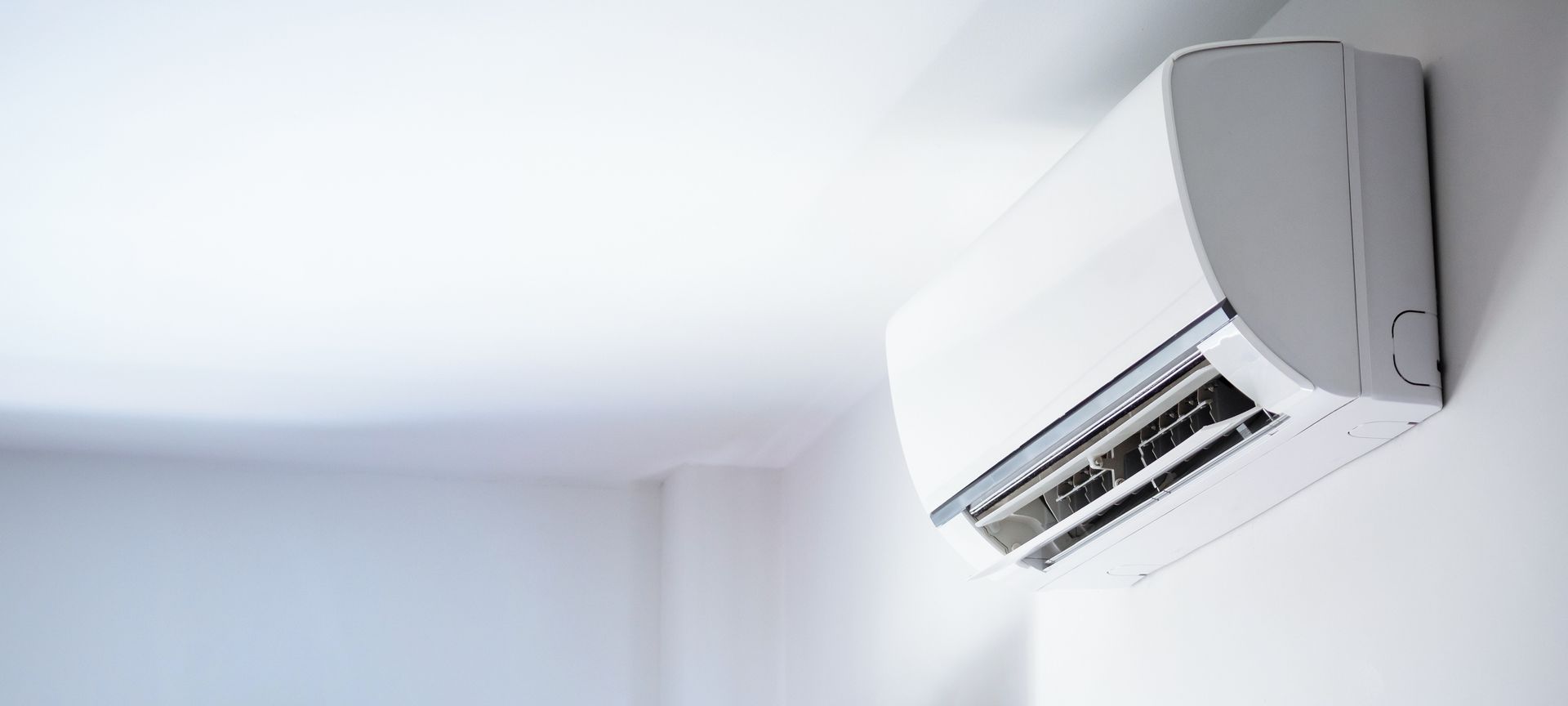 A white air conditioner is hanging on a white wall in a room.