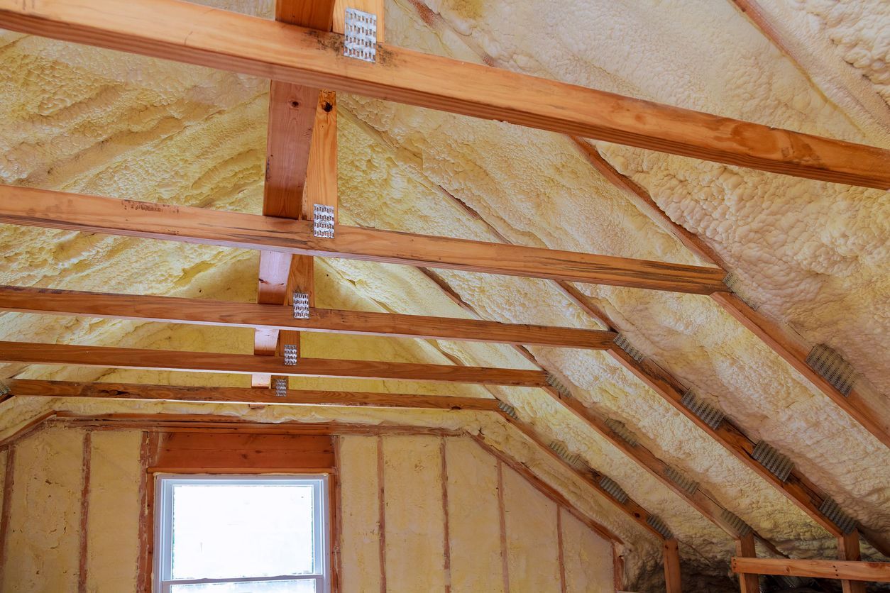 The ceiling of an attic with wooden beams and insulation.