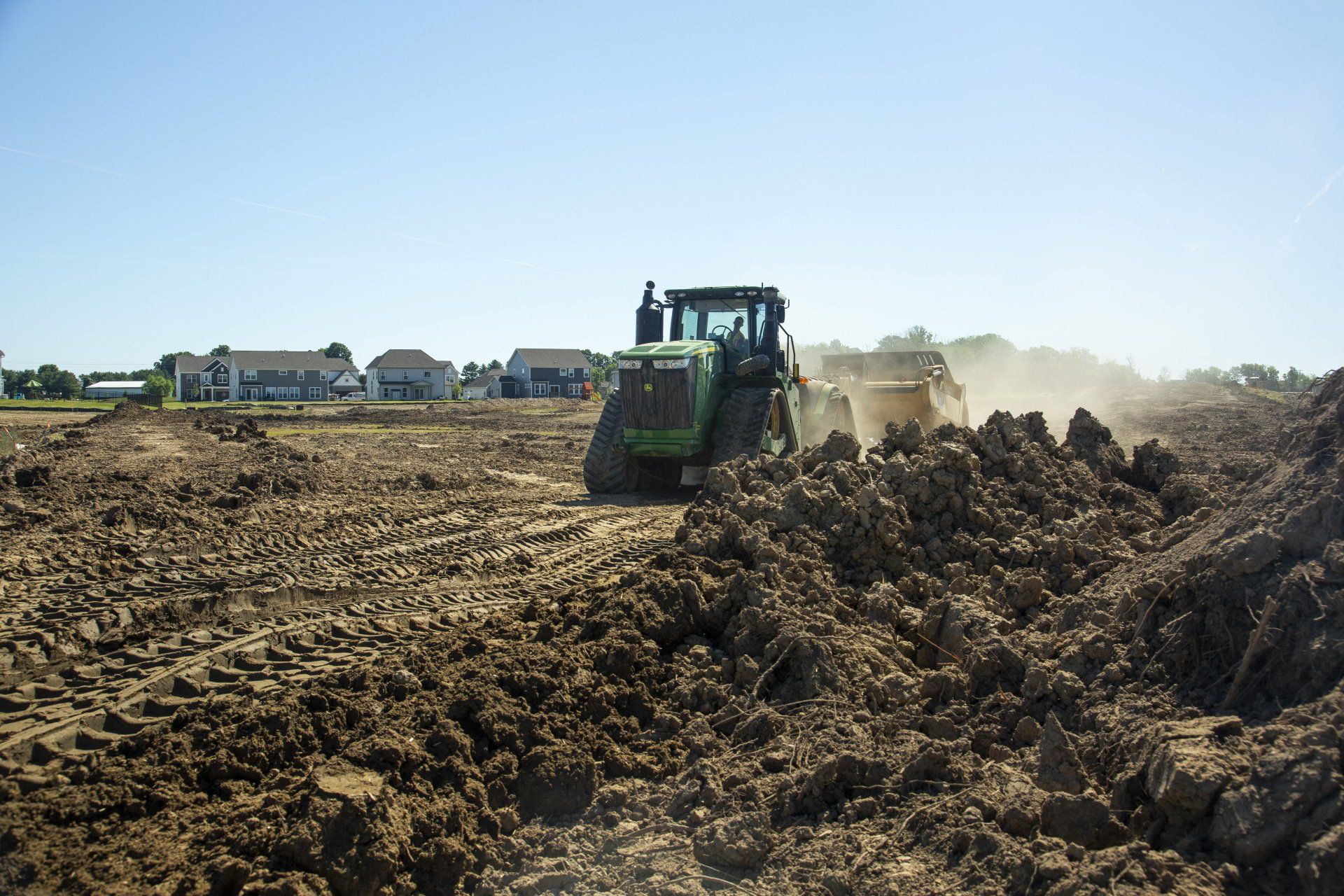 A green tractor is plowing a dirt field.