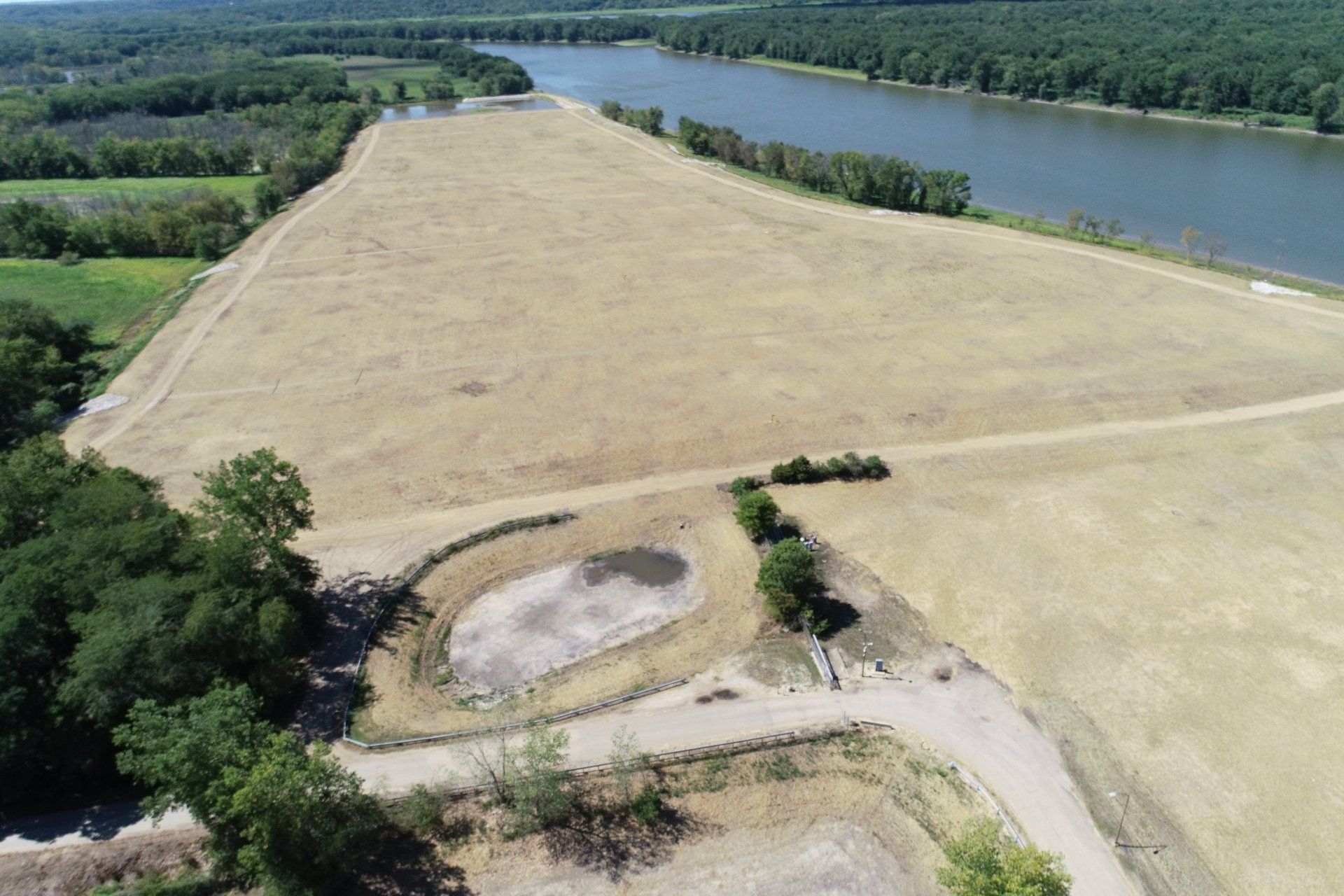 An aerial view of a field next to a river surrounded by trees.