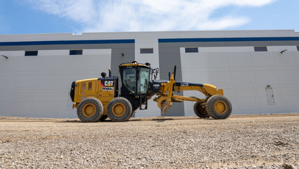 A bulldozer is driving down a dirt road in front of a building.