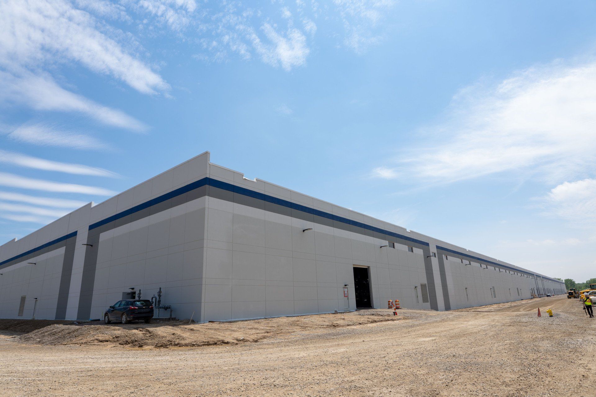 A large white building with a blue stripe on the side is sitting on top of a dirt field.