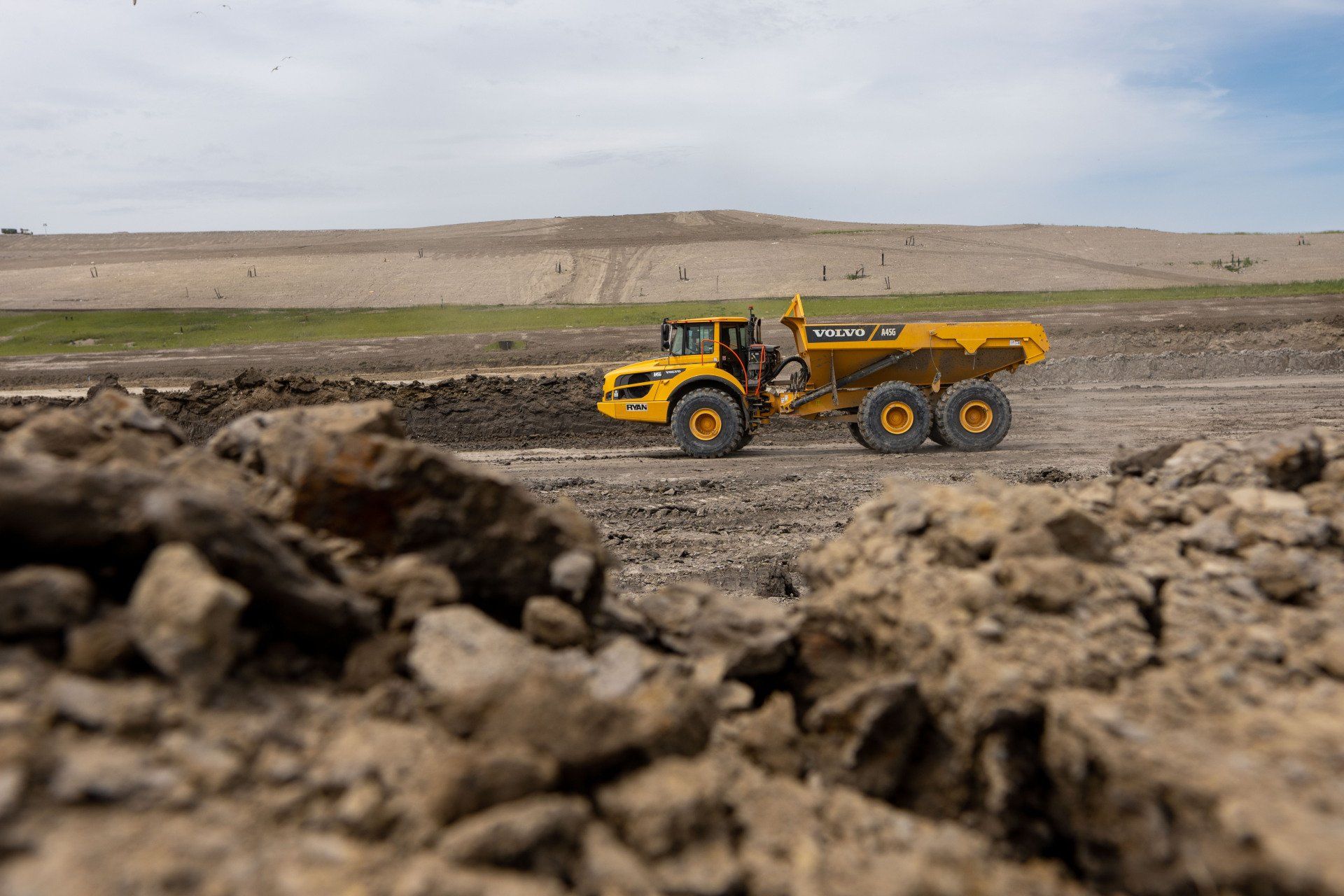 A yellow dump truck is driving through a dirt field.