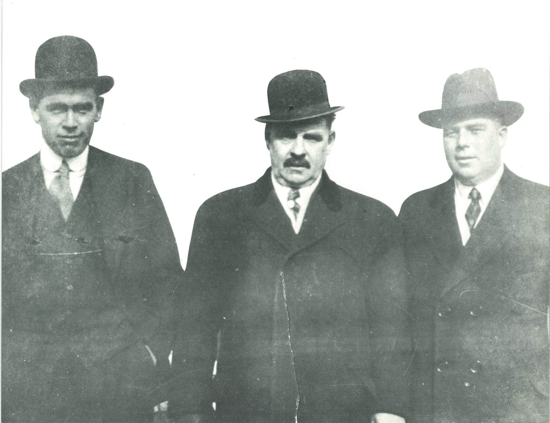 Three men in suits and hats are standing next to each other