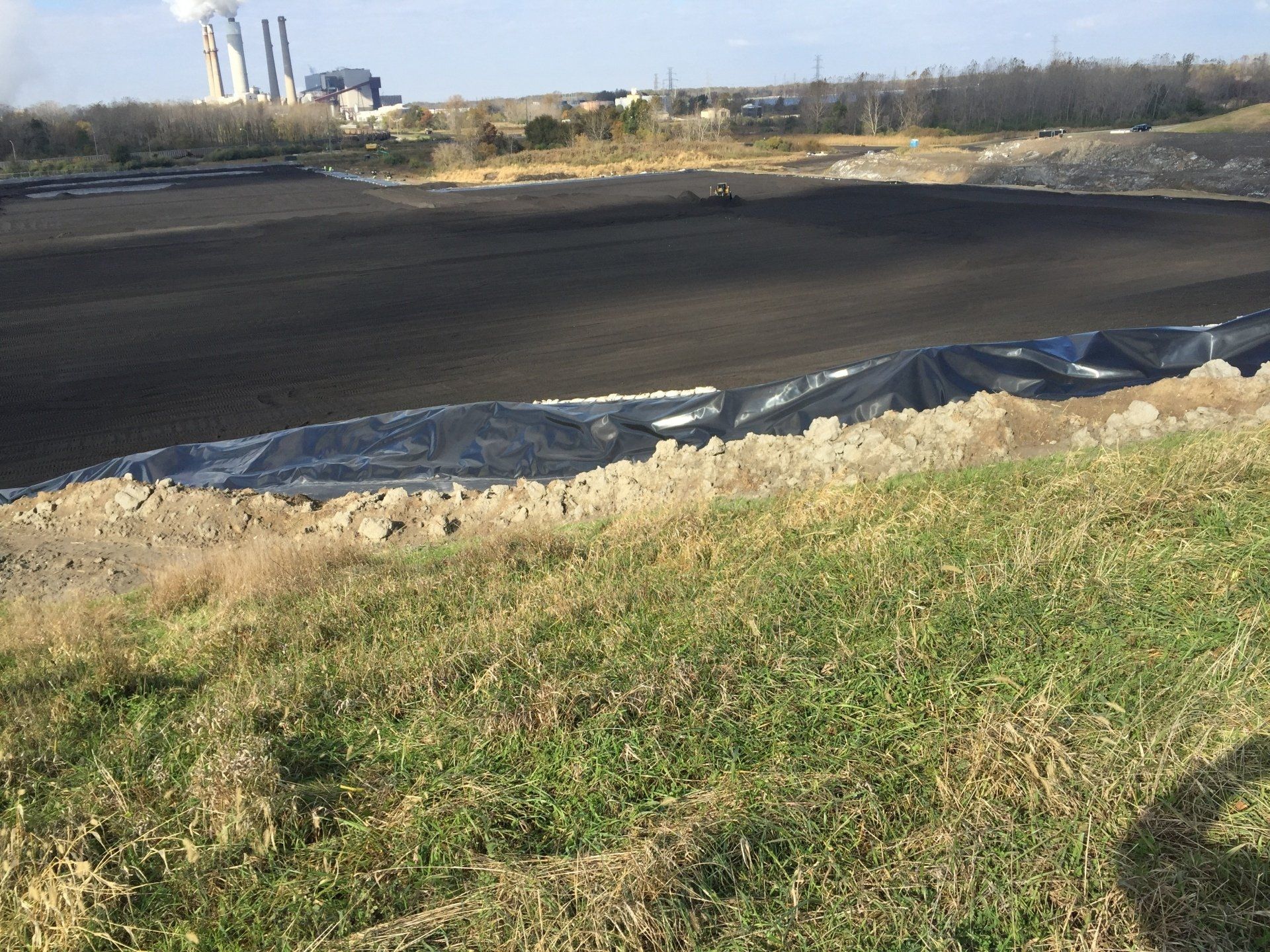 A large black tarp is covering a field with a factory in the background.