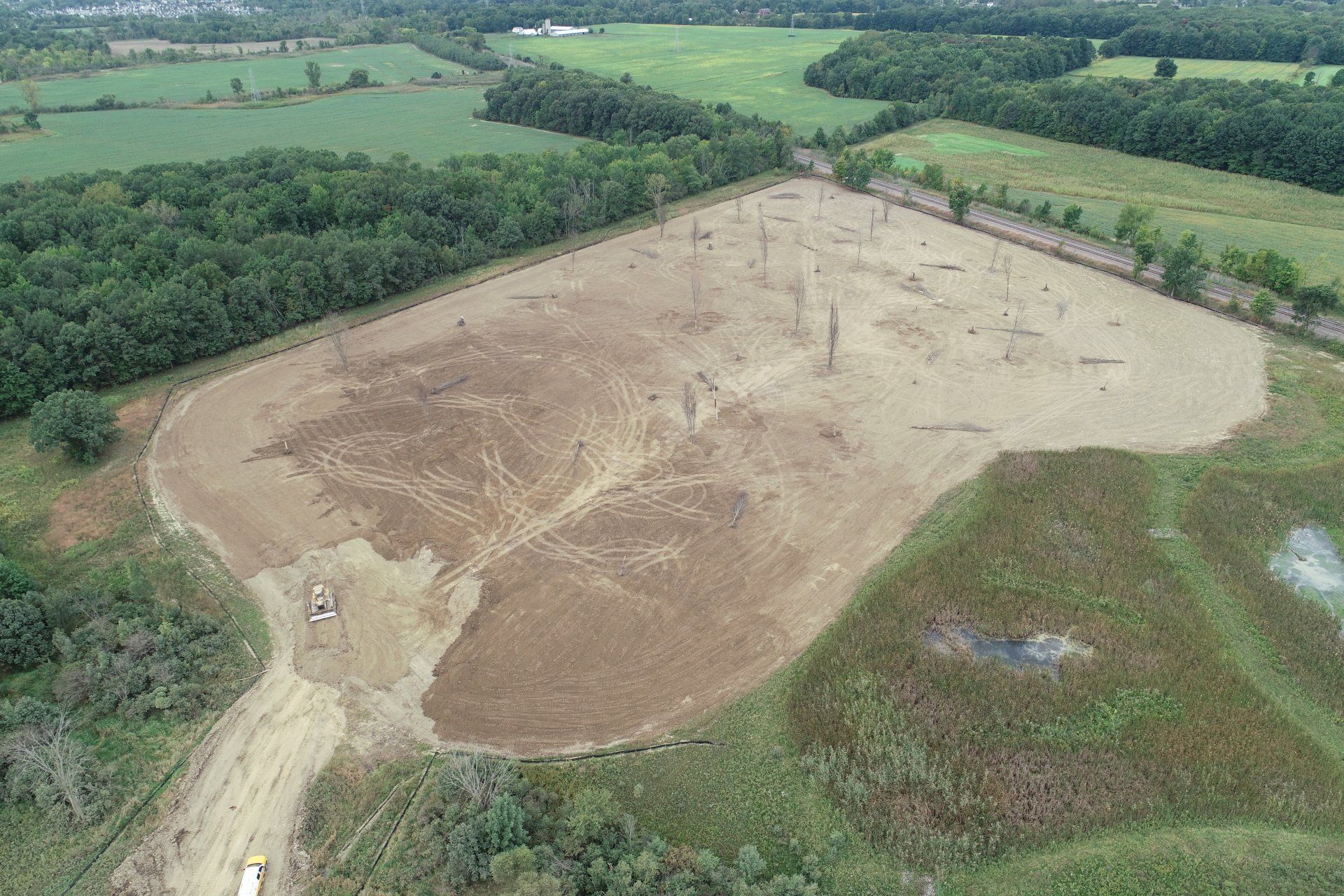 An aerial view of a large dirt field surrounded by trees and fields.