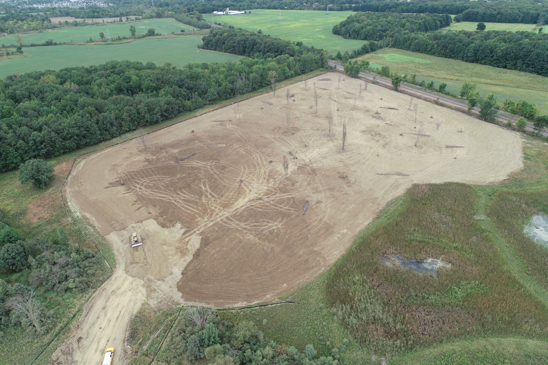An aerial view of a large dirt field surrounded by trees and fields.