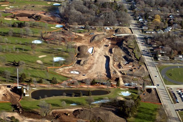 An aerial view of a construction site surrounded by trees and a road.