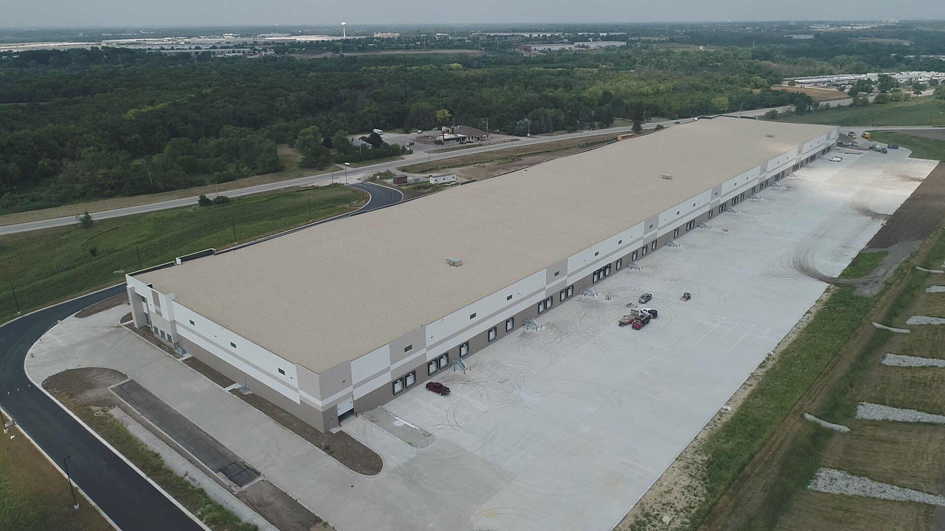 An aerial view of a large warehouse surrounded by trees and a road.