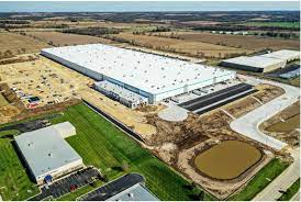 An aerial view of a large warehouse in a industrial area surrounded by fields.