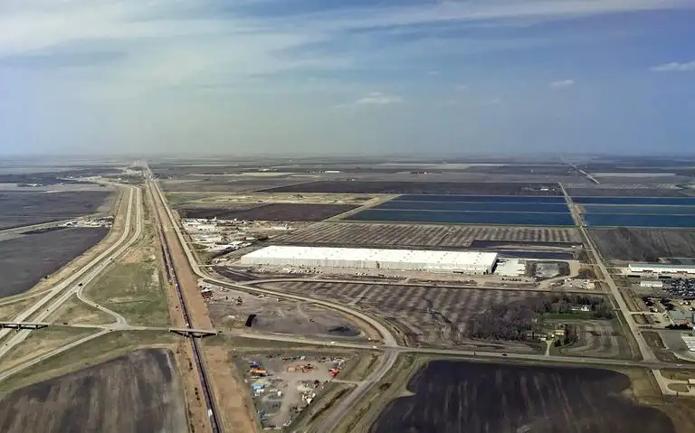 An aerial view of a large white building surrounded by fields and a highway.