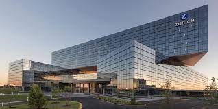 A large glass building with a lot of windows is surrounded by trees and grass.
