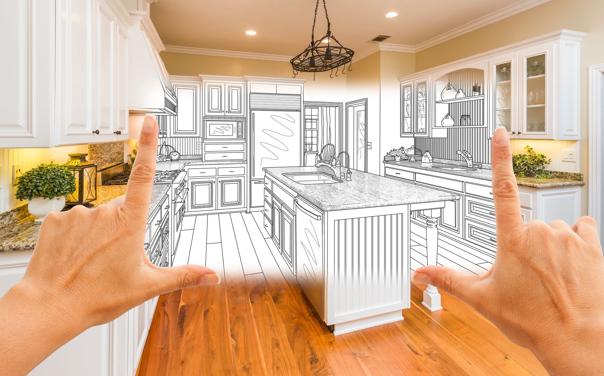 Hands framing a modern kitchen remodeling concept sketch over a real wooden floor photo.