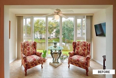Sunroom with two floral armchairs, a small table, a ceiling fan, and a view of a lake.