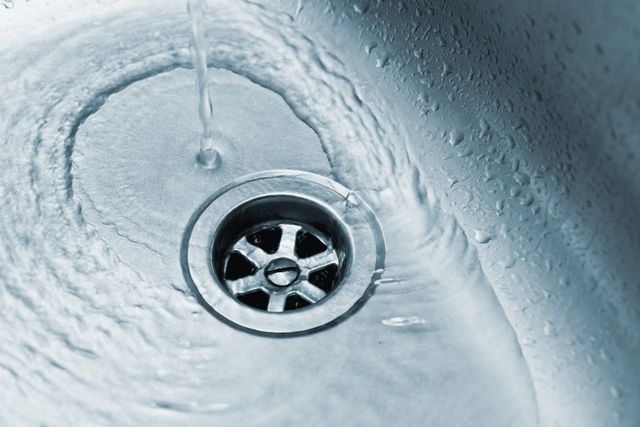 Water swirling down a metallic sink drain.
