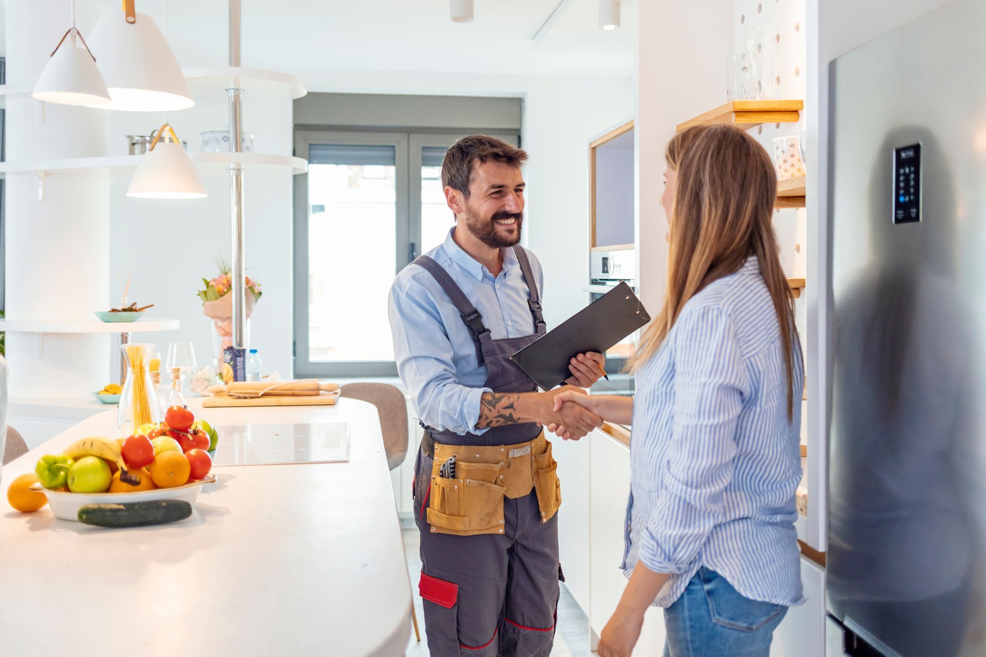 Handyman shaking hands with a woman in a bright kitchen.
