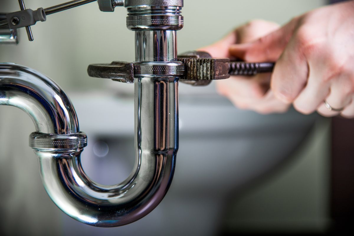 Plumber using a wrench to tighten a pipe beneath a sink.