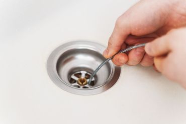 Hand opening a bathroom sink drain with a metal tool