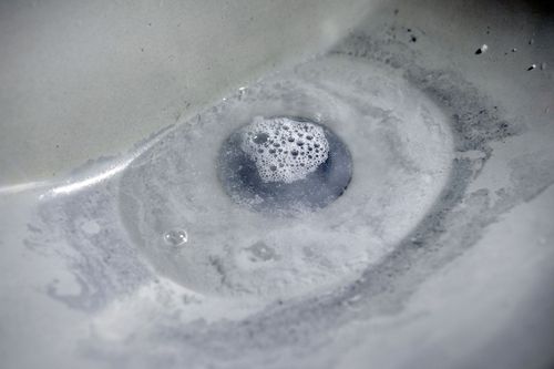 Close-up of a silver sink drain with a foamy bubble in the center and water residue around it