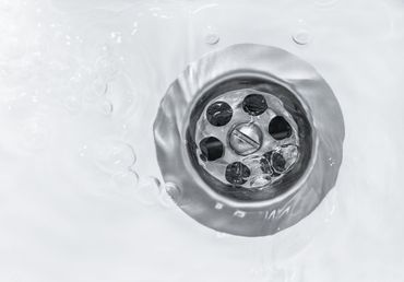 Close-up of a silver sink drain with water swirling around it on a white surface