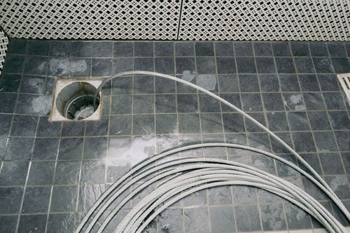 Coiled white cable leading into a floor opening on a dark tiled surface.