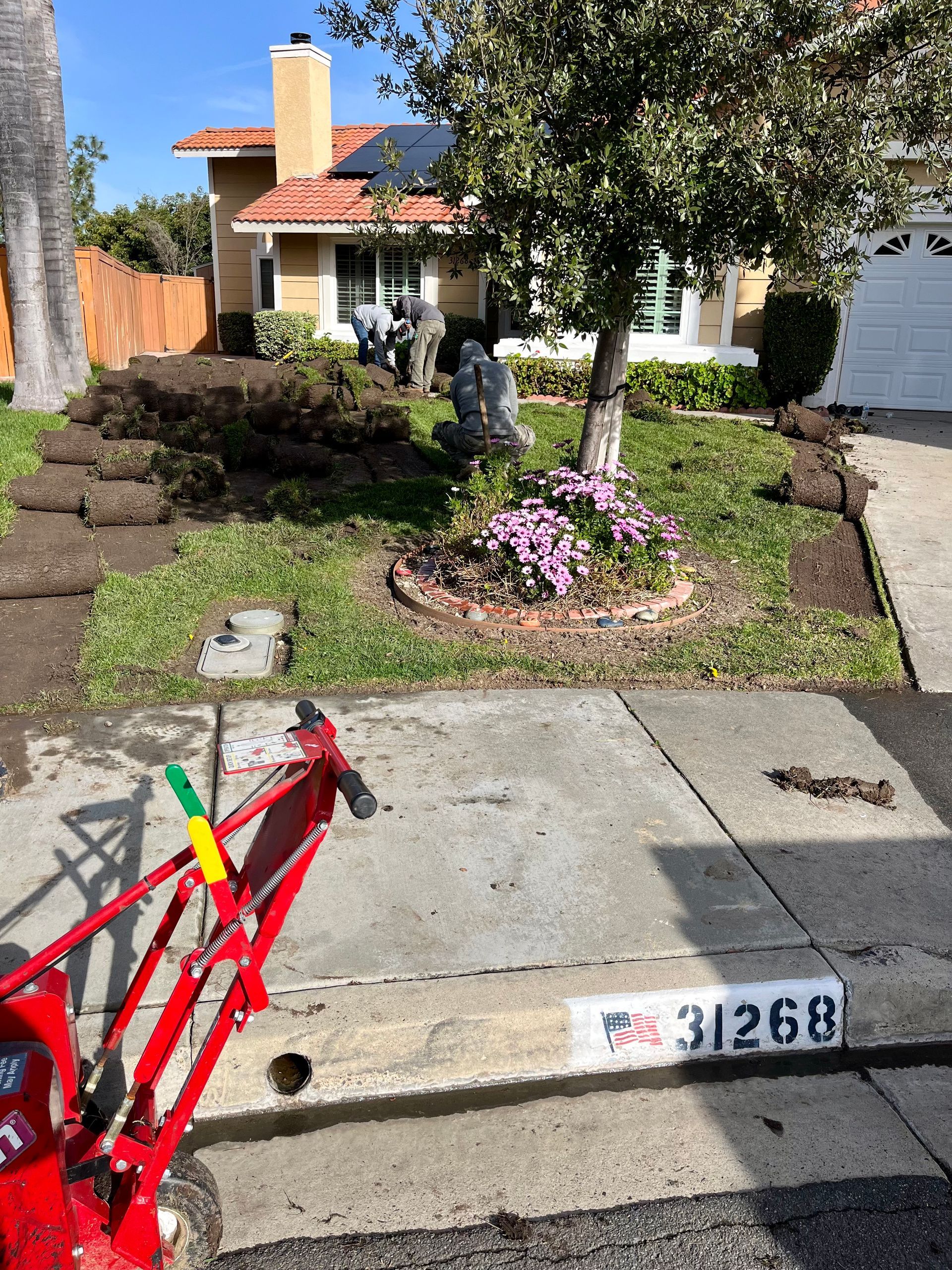 A red lawn mower is parked on the sidewalk in front of a house.