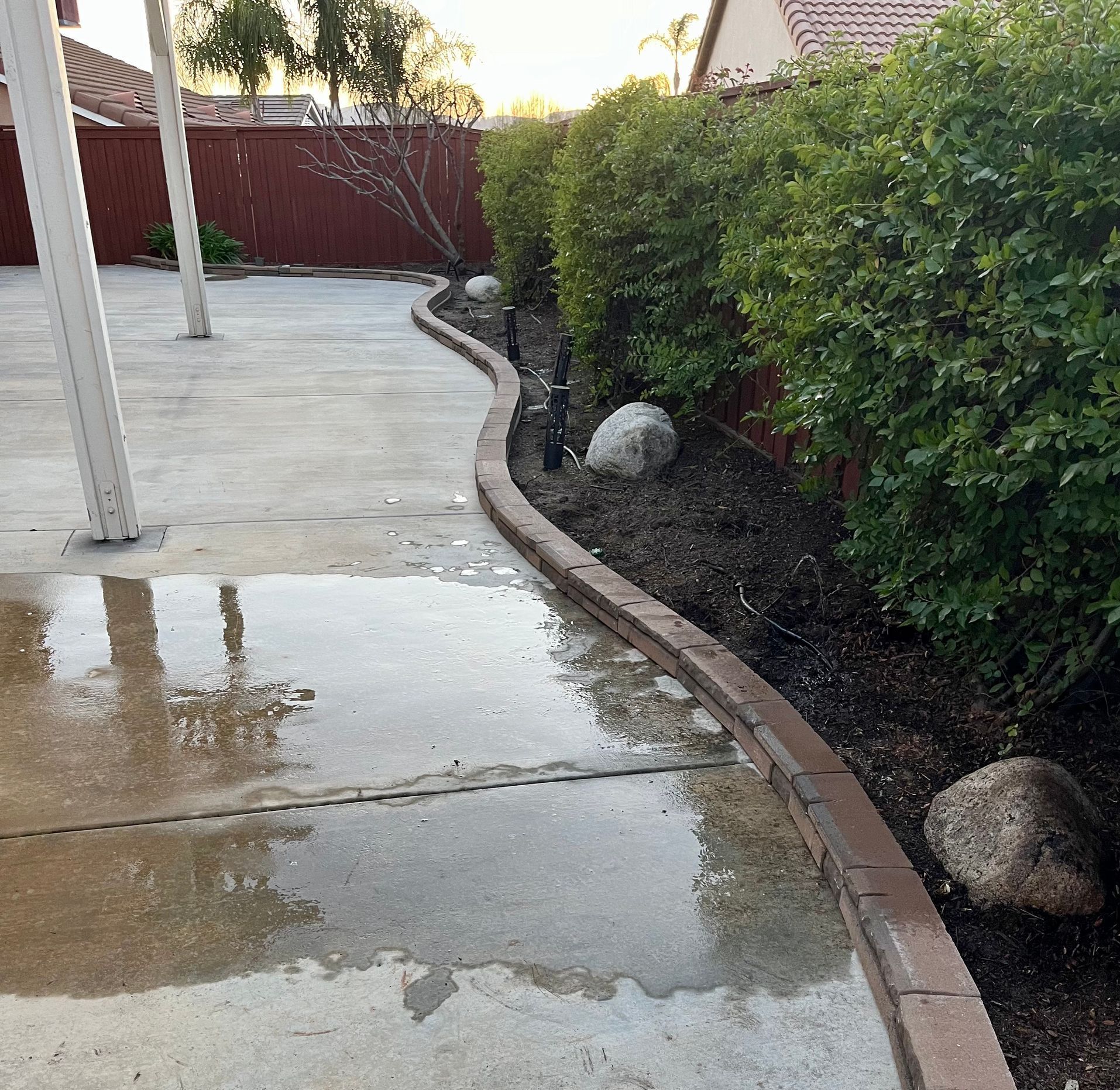 A concrete walkway with a brick border and a reflection of trees in the water.