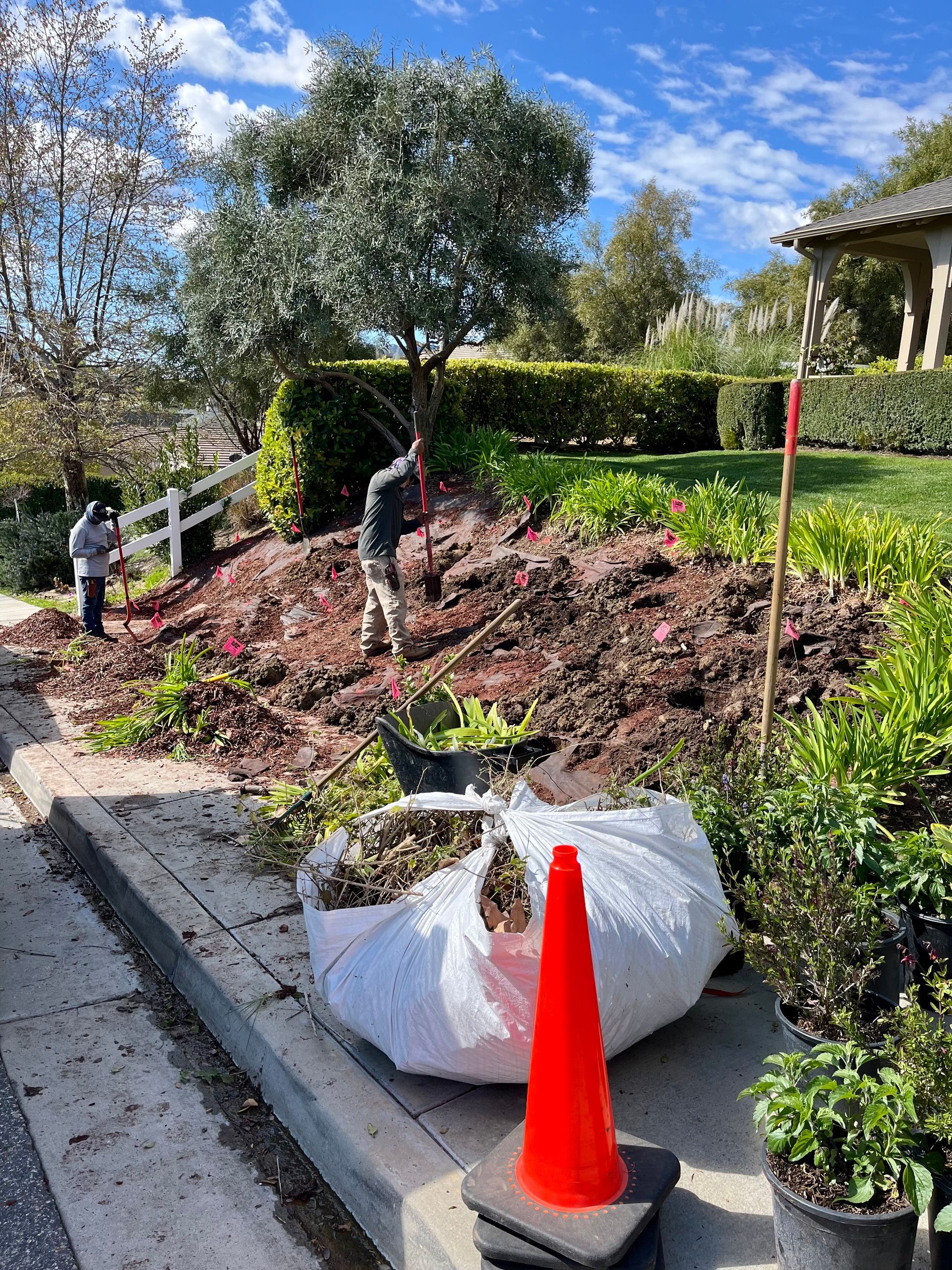 A large bag of mulch is sitting on the side of the road next to an orange cone.