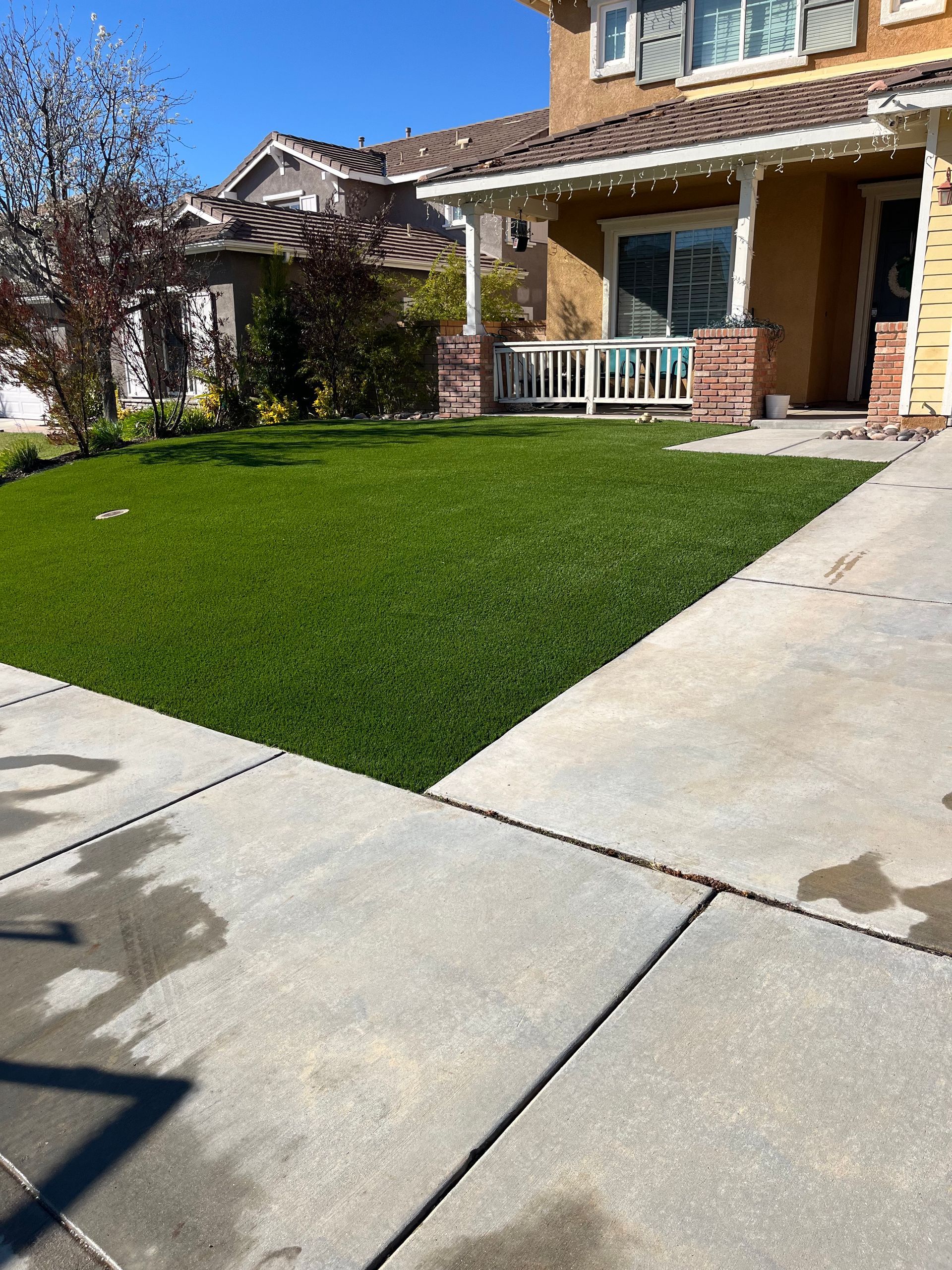 Suburban house with a covered porch, green lawn, and concrete driveway under a clear blue sky